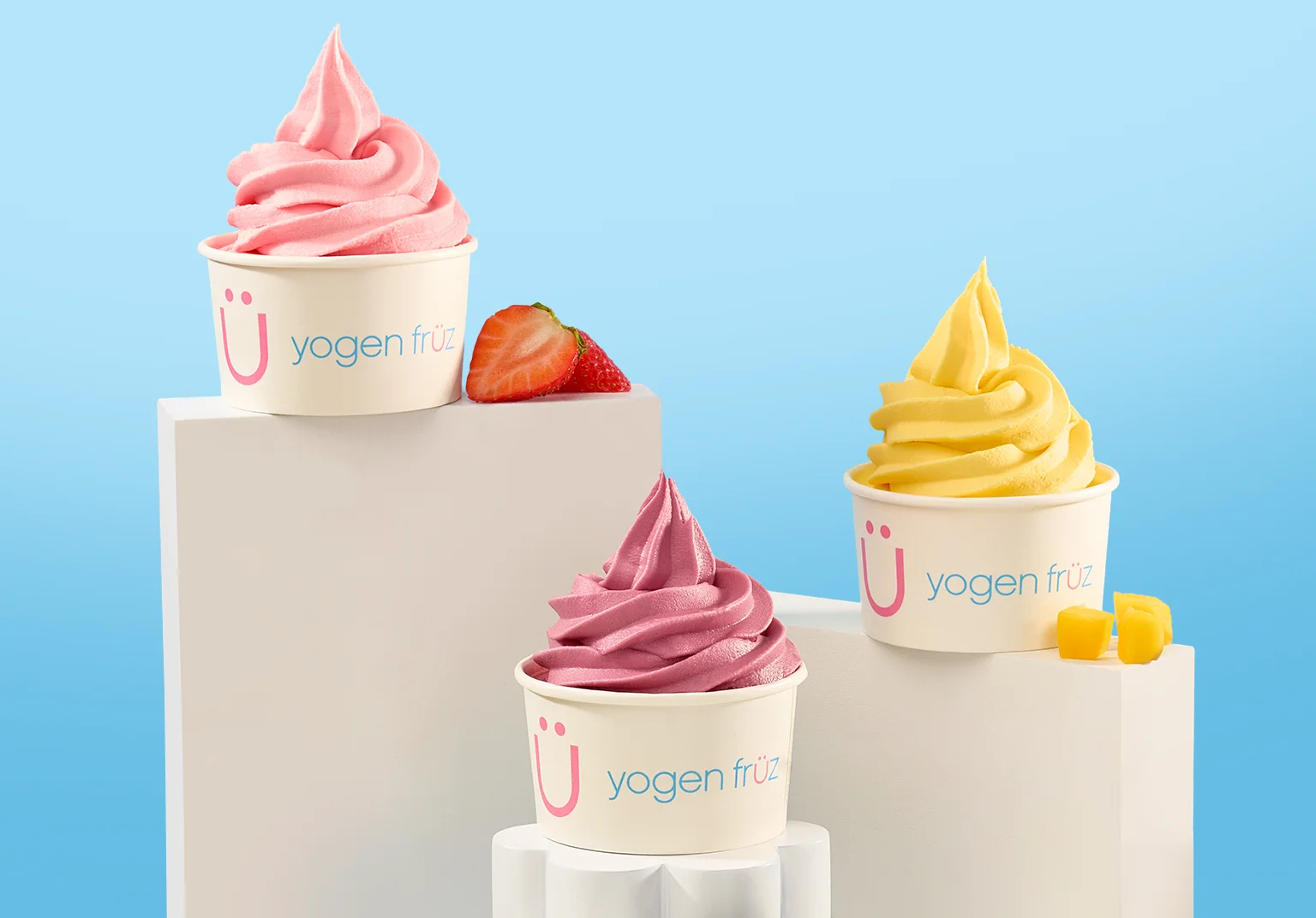 Three cups of Yogen Früz frozen yogurt — strawberry, mixed berry and mango — with fresh fruit beside them