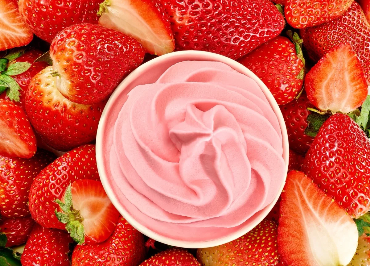 A cup of strawberry frozen yogurt surrounded by fresh strawberries